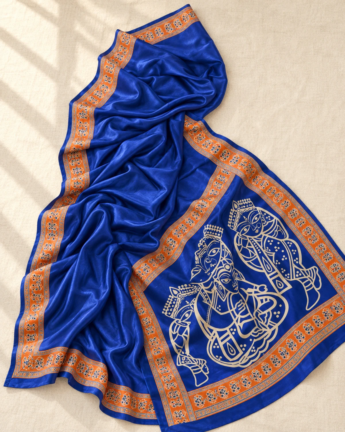 The royal blue modal satin saree laid out flat, showing its orange Ajrakh border and figure pallu