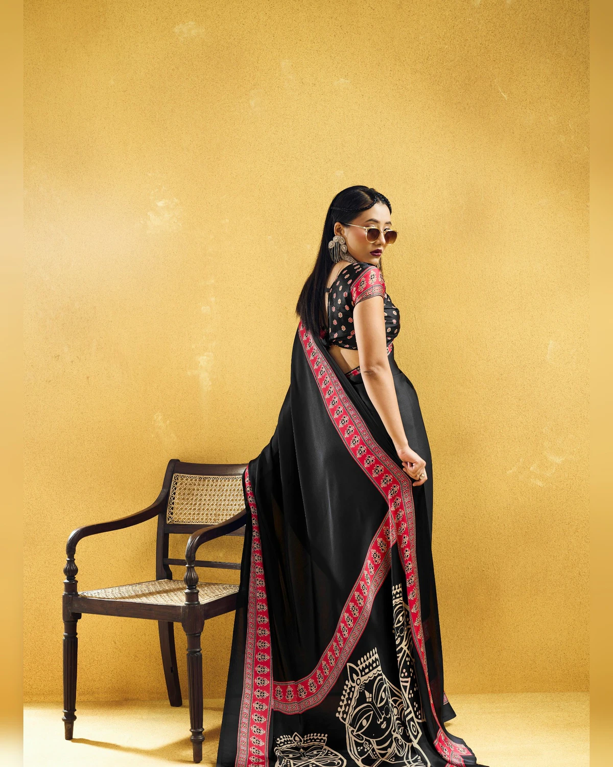 Woman in the black modal satin saree seen from the back, its red-bordered pallu falling behind her