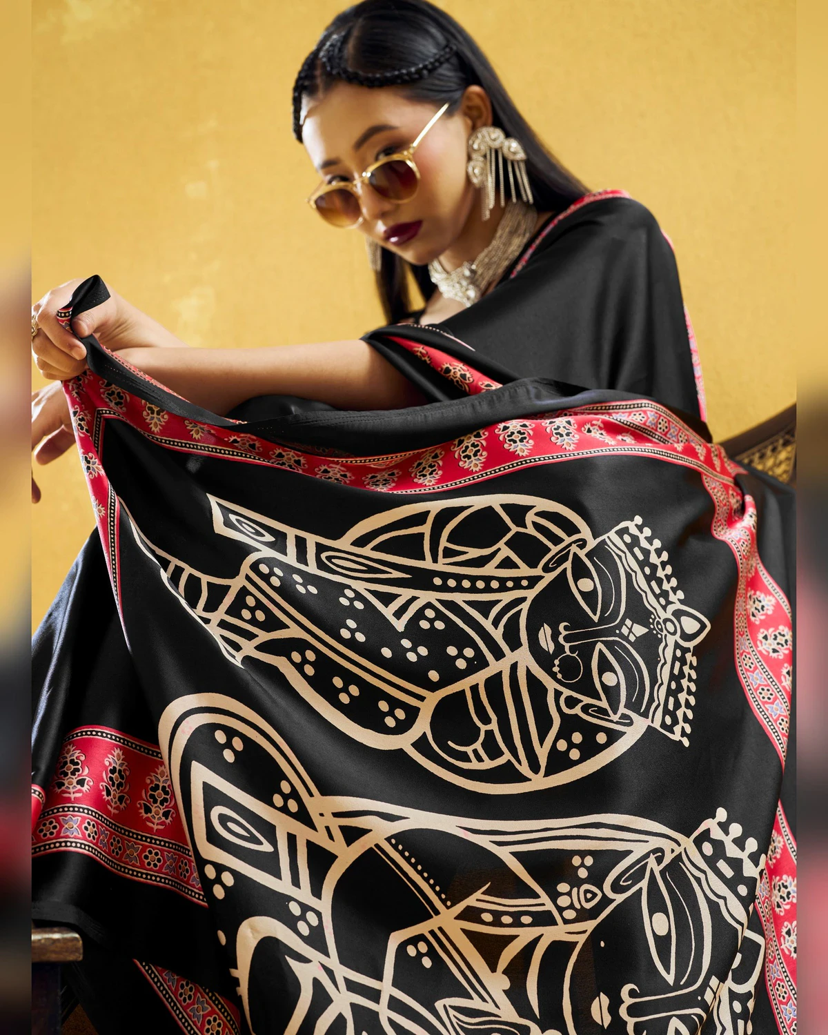 Woman holding out the black saree's pallu to show its large cream line-drawn figures
