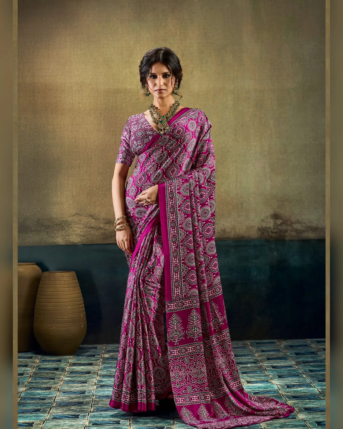 Woman wearing a plum all-over Ajrakh print modal satin saree, standing by clay pots on a blue tiled floor
