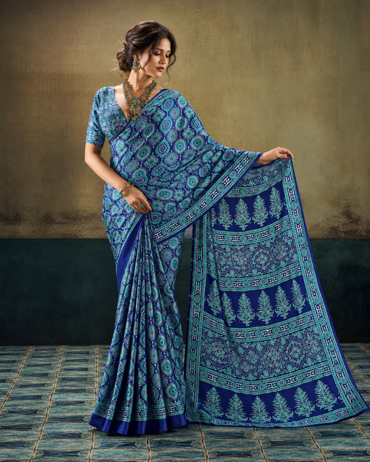 Woman holding out the blue saree's pallu to show its rows of tree-shaped butas
