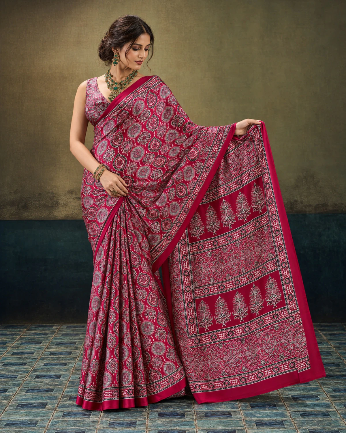 Woman holding out the crimson saree's pallu to show its rows of tree-shaped butas