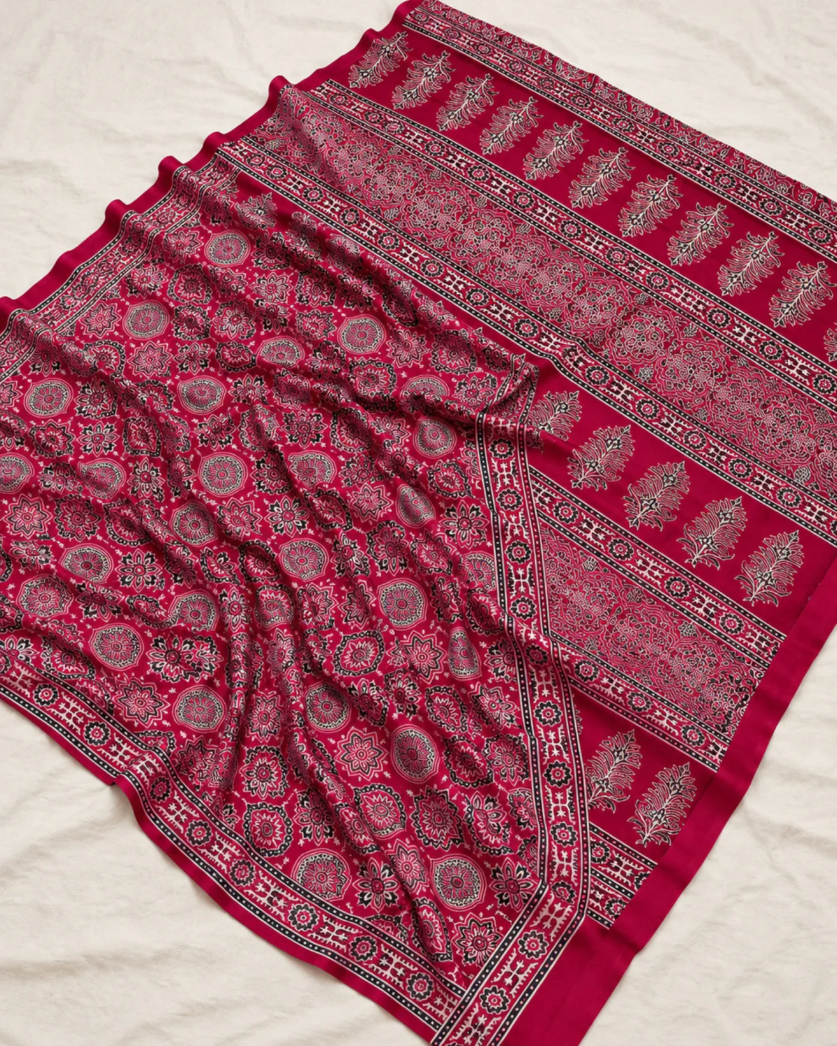 The crimson modal satin saree laid out flat, showing its pink and white Ajrakh medallions and buta pallu