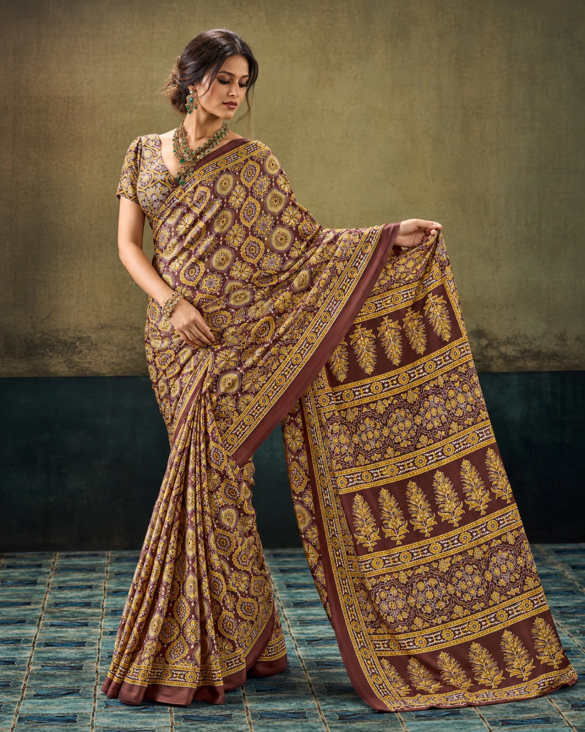 Woman holding out the brown saree's pallu to show its rows of tree-shaped butas