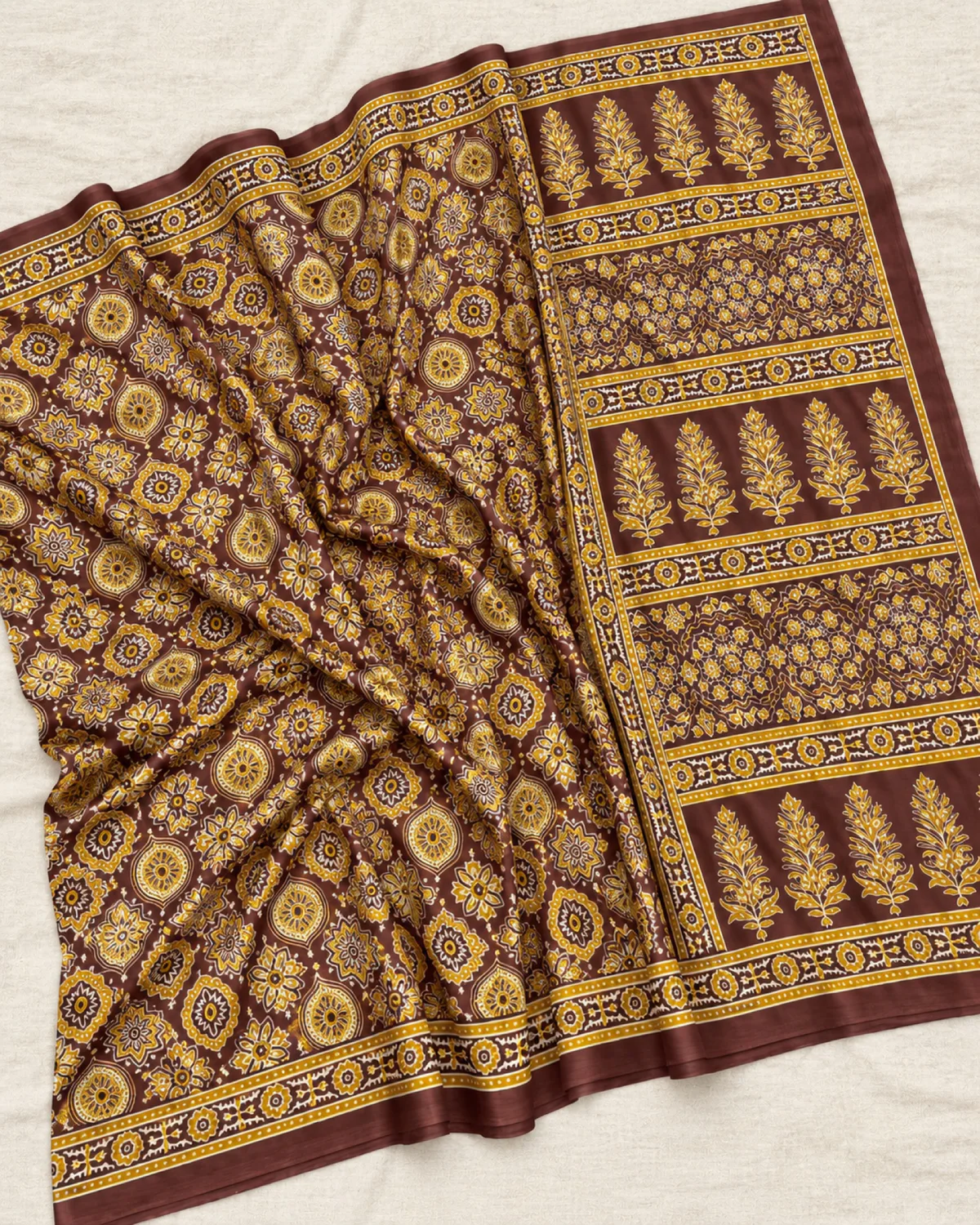 The brown modal satin saree laid out flat, showing its mustard and gold Ajrakh medallions and buta pallu
