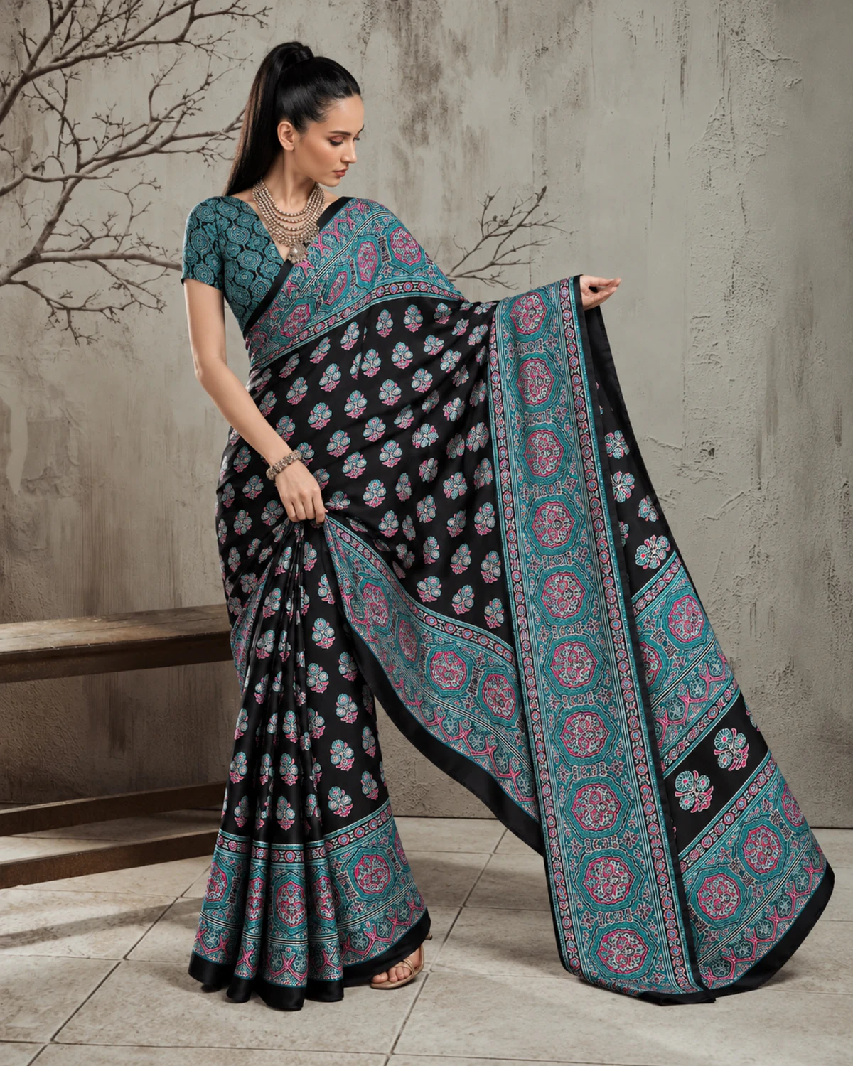 Woman holding out the black and teal saree's pallu to show its wide teal Ajrakh border
