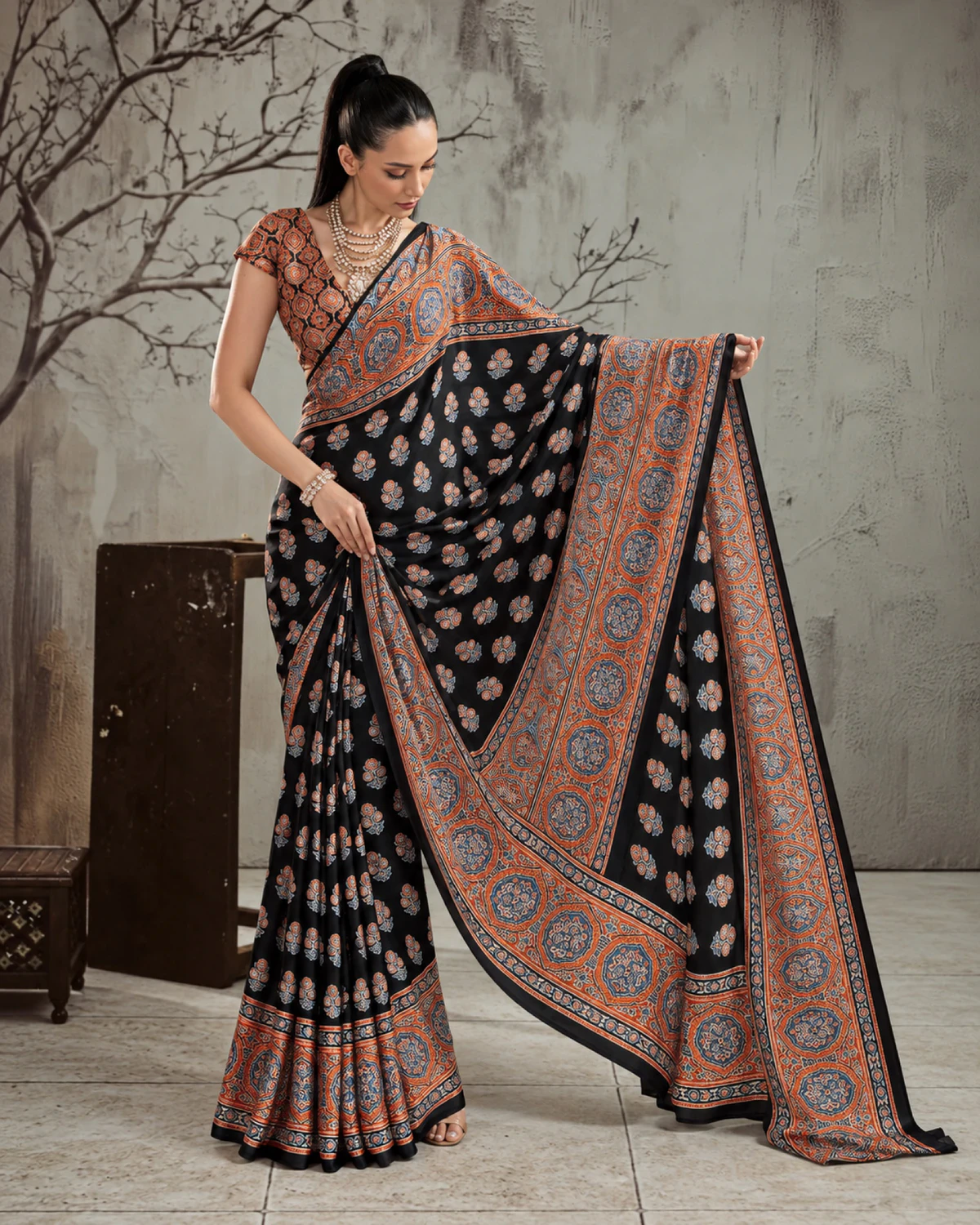 Woman holding out the black and rust saree's pallu to show its wide rust Ajrakh border
