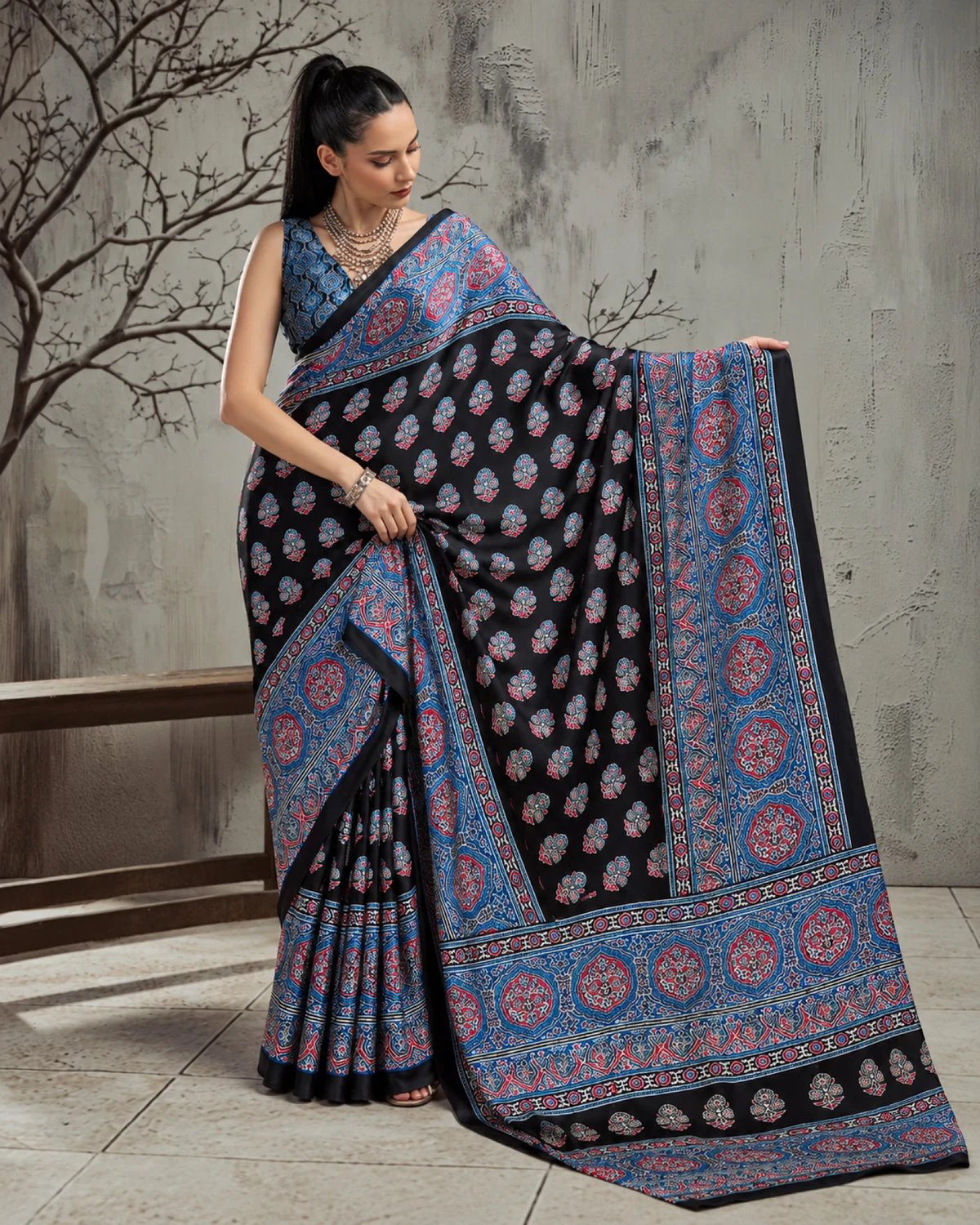 Woman holding out the black and blue saree's pallu to show its wide blue Ajrakh border