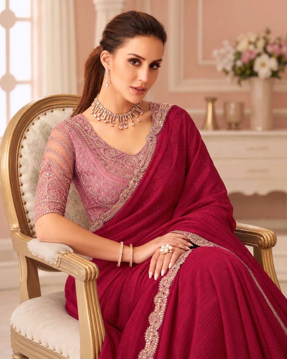 Woman in the wine georgette saree and a dusty pink embroidered blouse, seated on a gold armchair