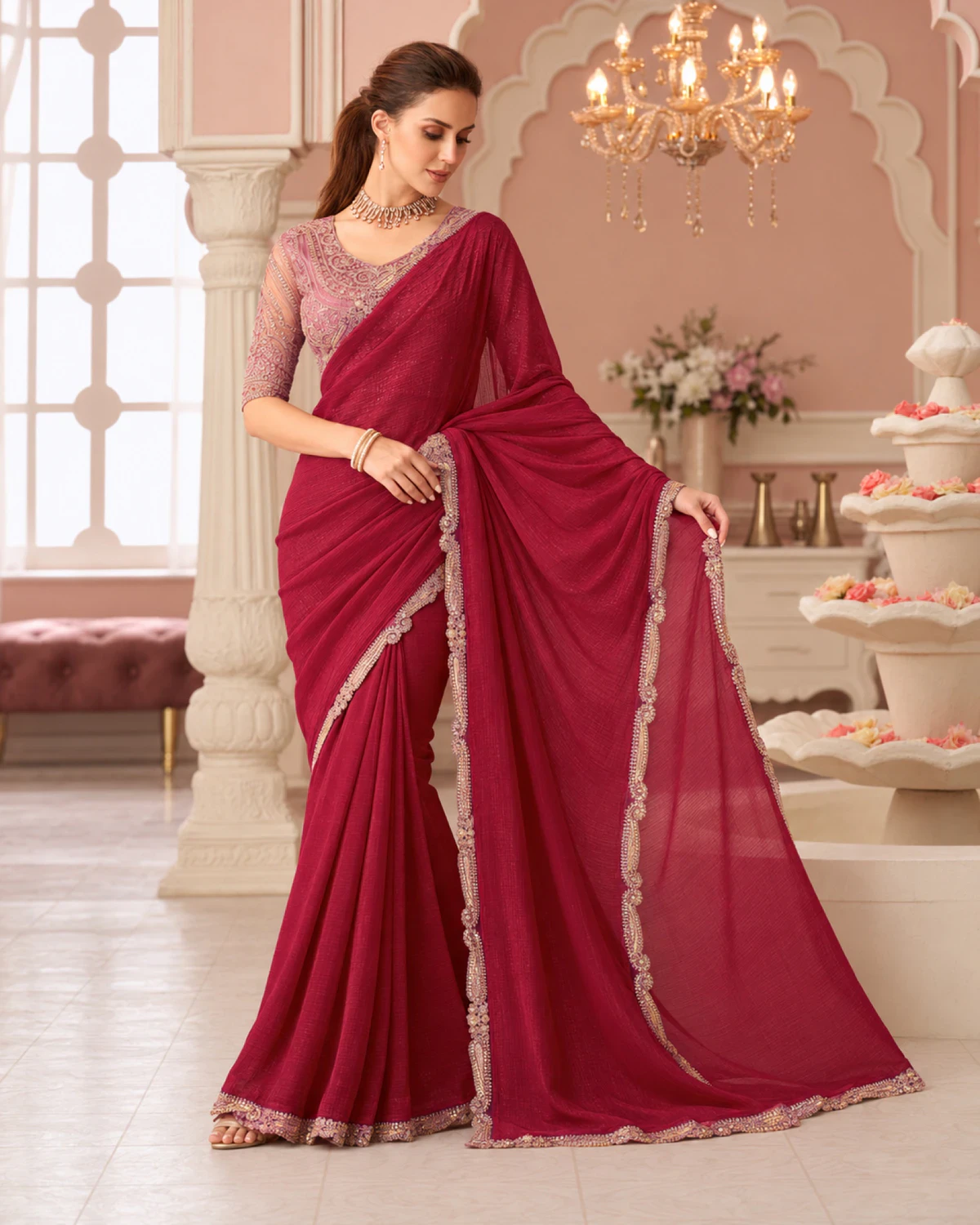 Woman holding out the pallu of the wine georgette saree under a chandelier