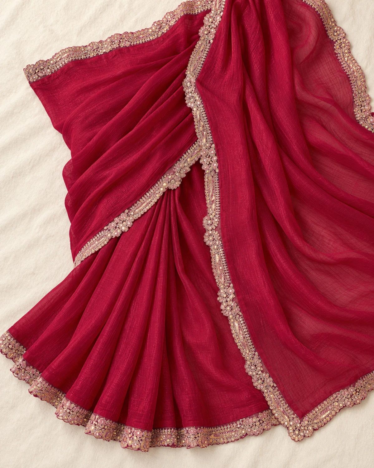 The wine georgette saree laid flat on a cream cloth, showing its scalloped rose-gold border