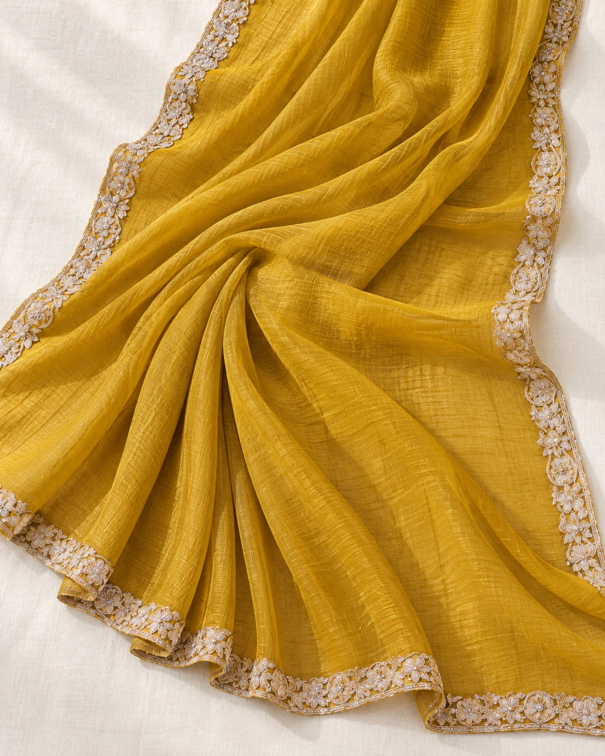 The mustard yellow georgette saree laid flat on a cream cloth, showing its scalloped ivory border