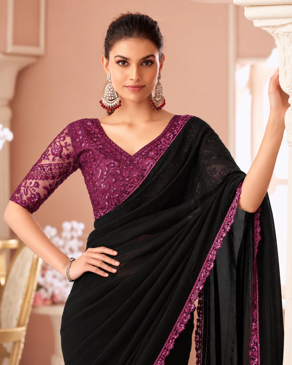 Woman in the black georgette saree and a magenta embroidered blouse, resting a hand on a carved pillar