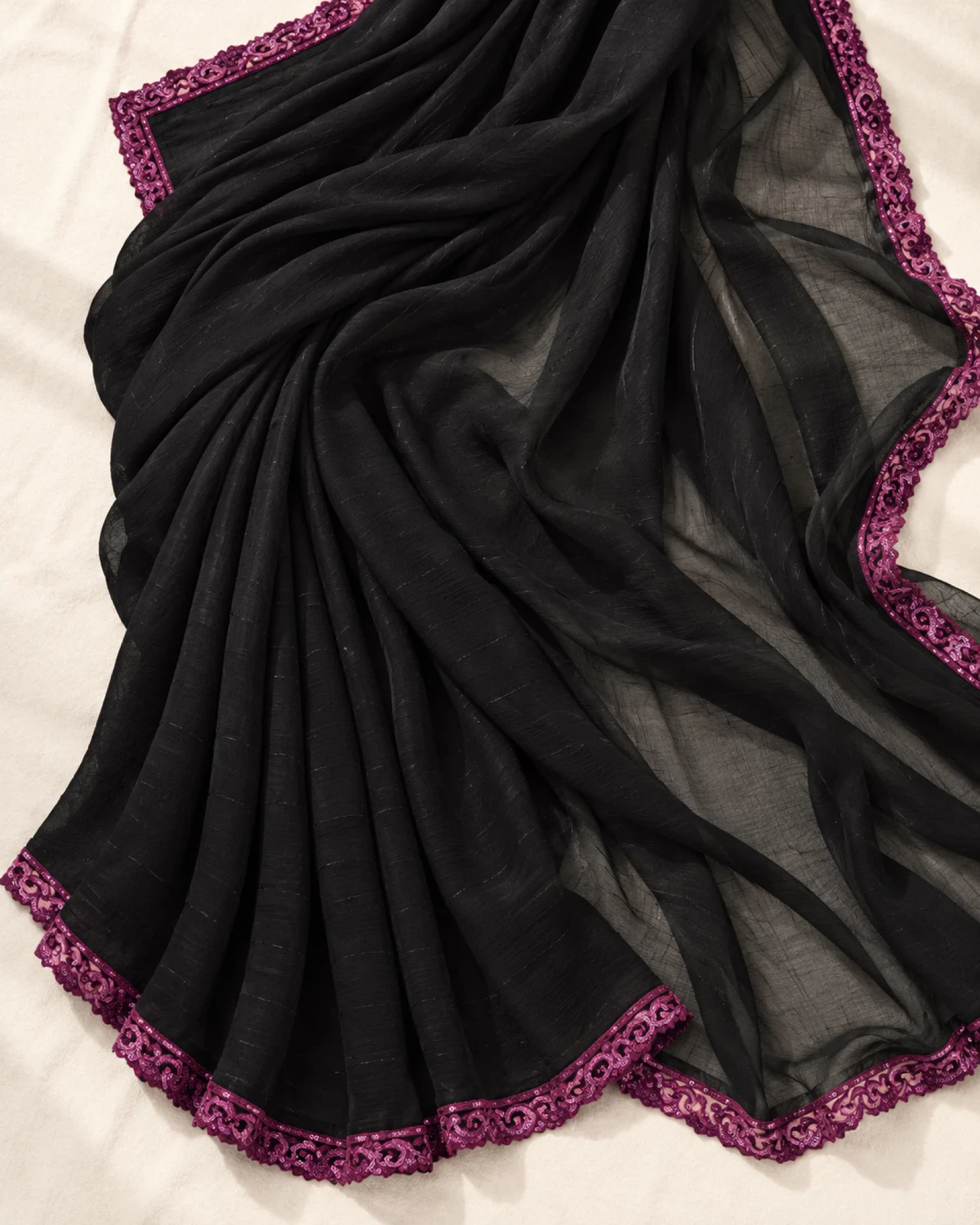 The black georgette saree laid flat on a cream cloth, showing its scalloped magenta border
