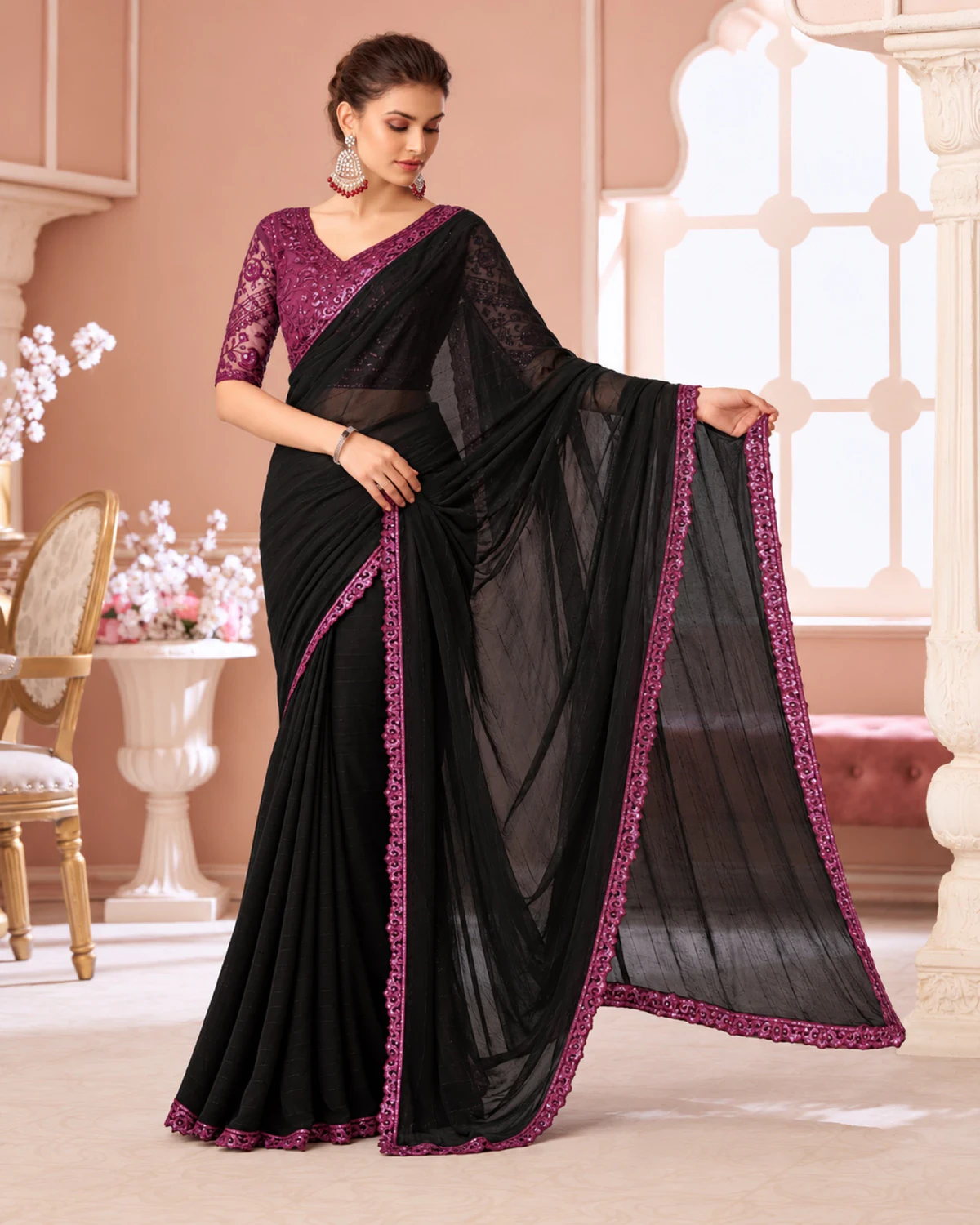 Woman holding out the pallu of the black georgette saree, its magenta border along the edge