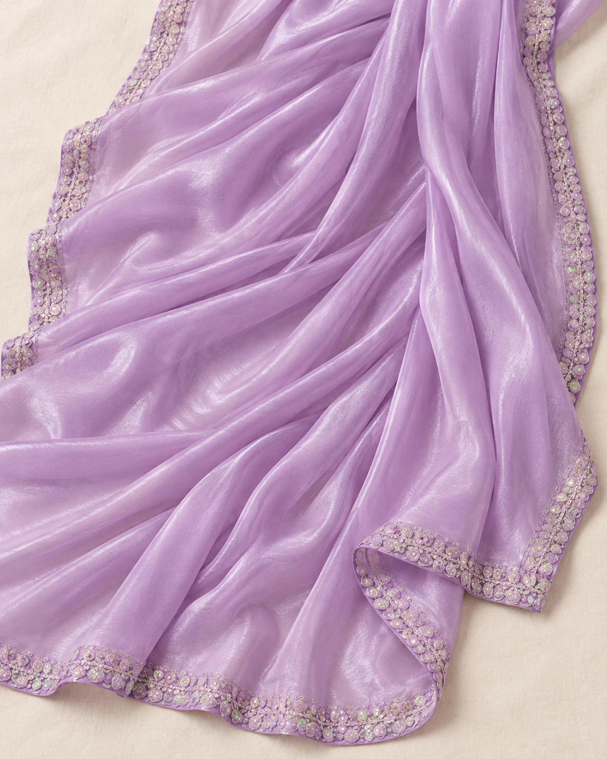 The lilac shimmer chiffon saree laid flat on a cream cloth, showing its shimmer and scalloped silver border
