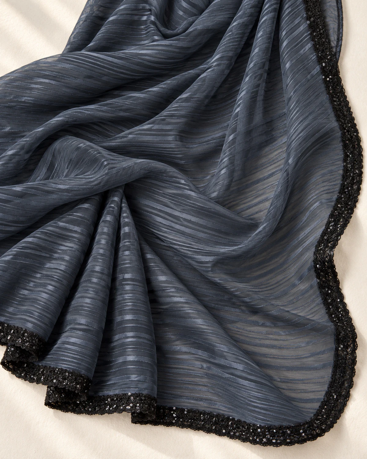 The charcoal grey georgette saree laid flat on a cream cloth, showing its wavy stripes and black border