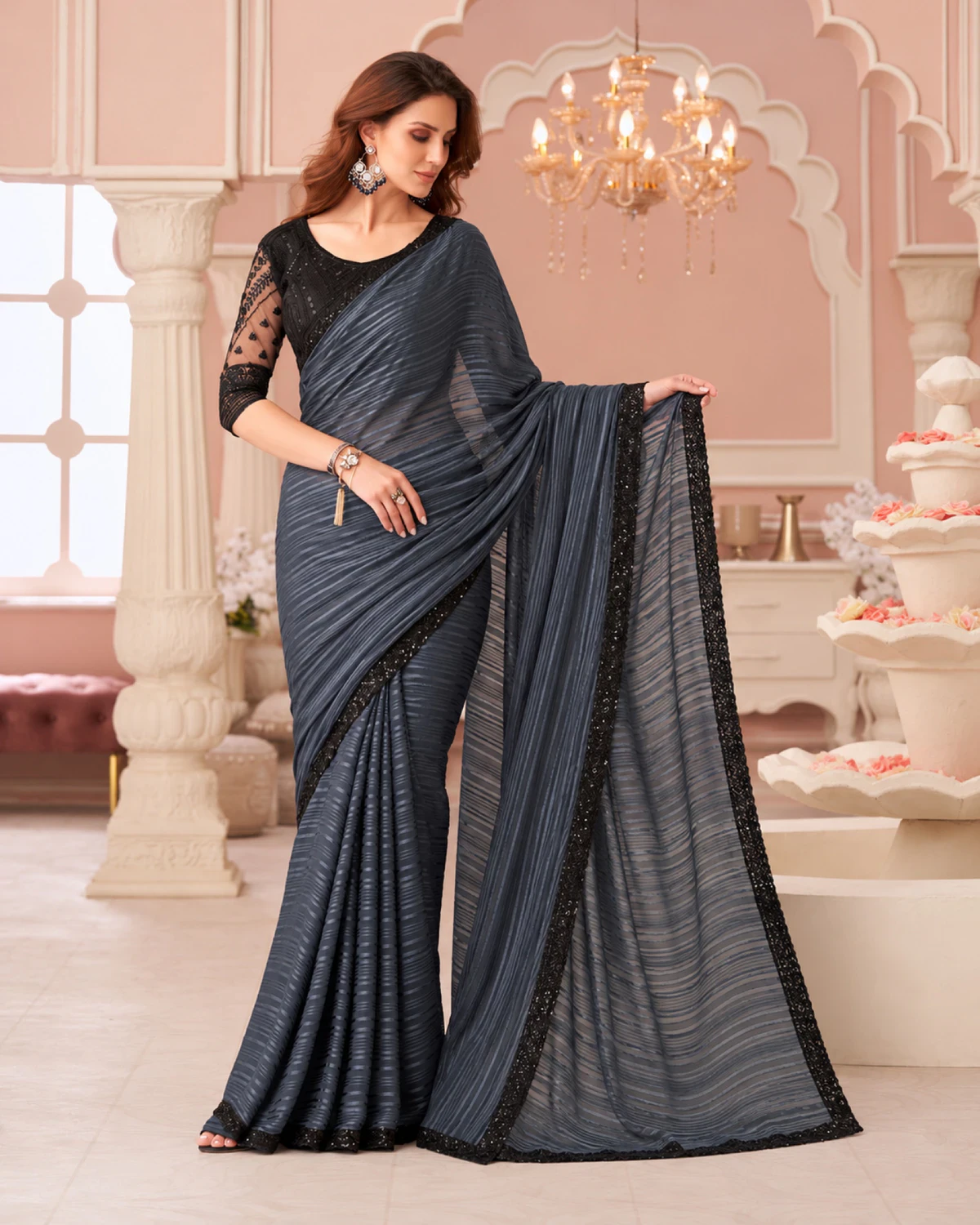 Woman holding out the pallu of the charcoal grey georgette saree under a chandelier