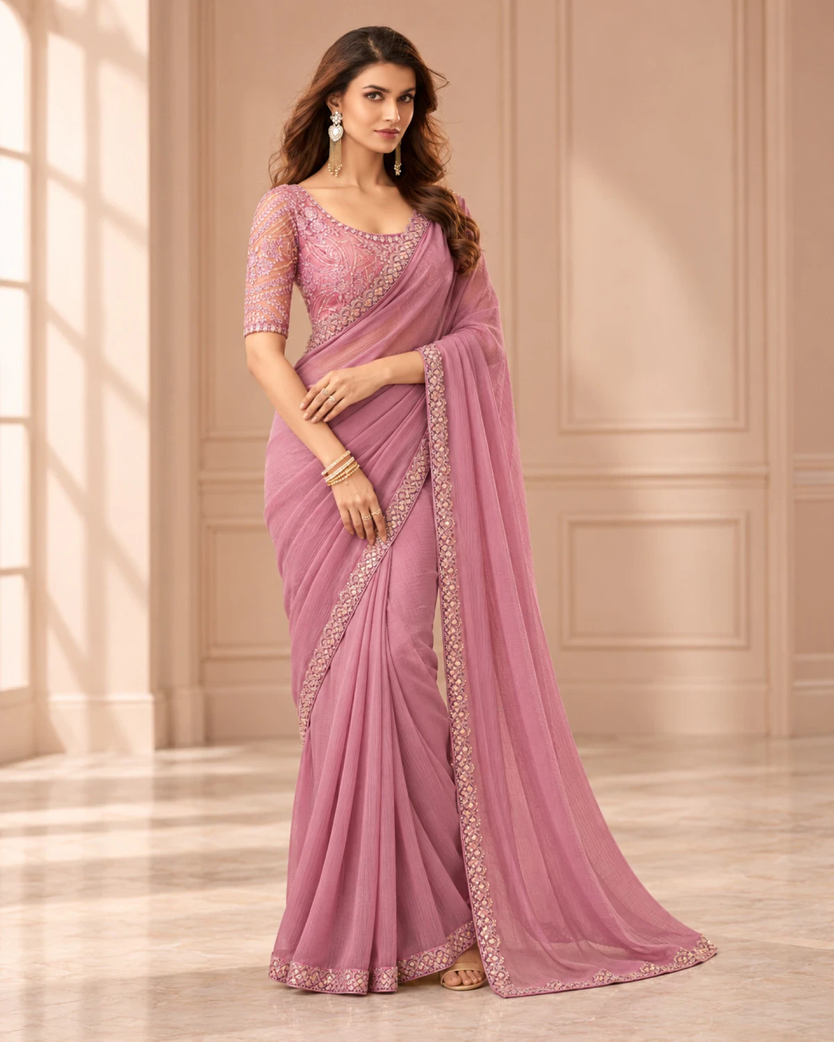 Woman wearing a dusty pink textured georgette saree with a matching border, standing in a softly lit peach room
