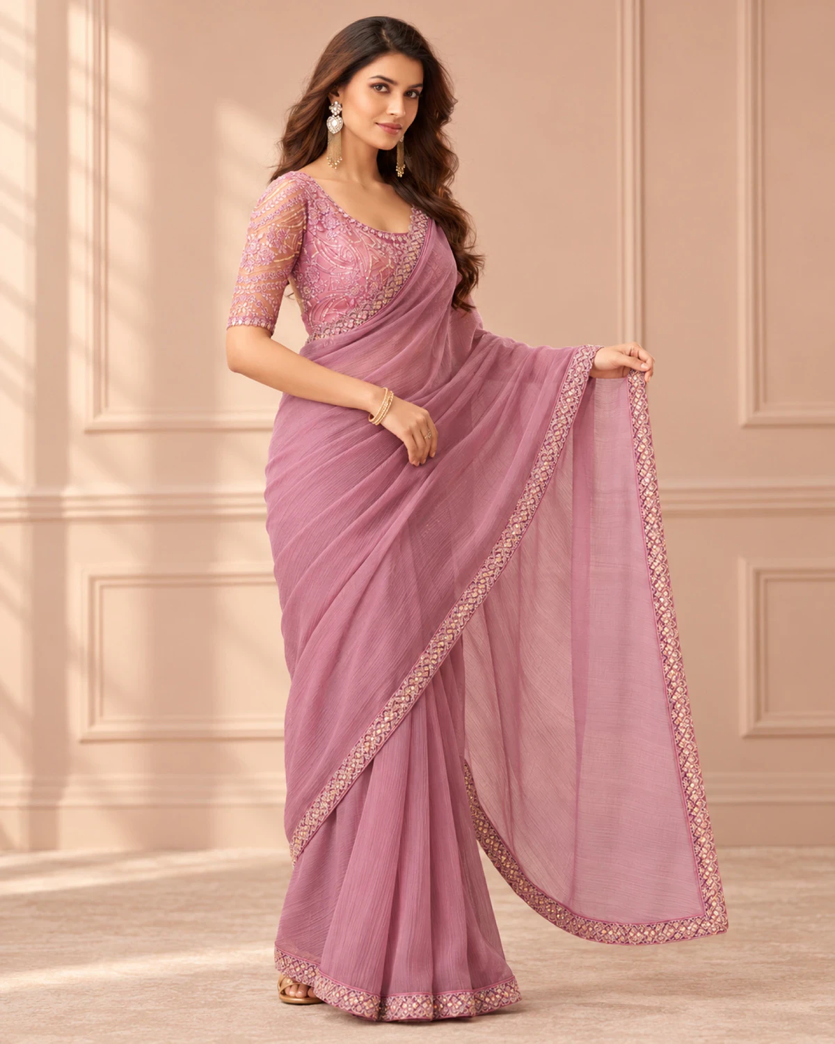 Woman holding out the pallu of the dusty pink georgette saree in a softly lit room