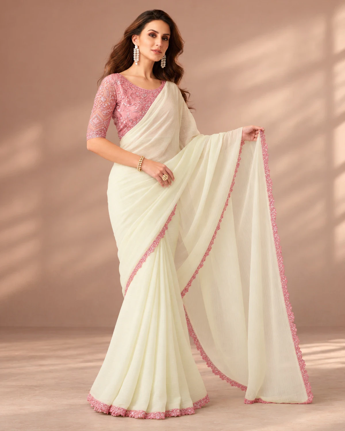 Woman holding out the pallu of the ivory georgette saree in a softly lit room