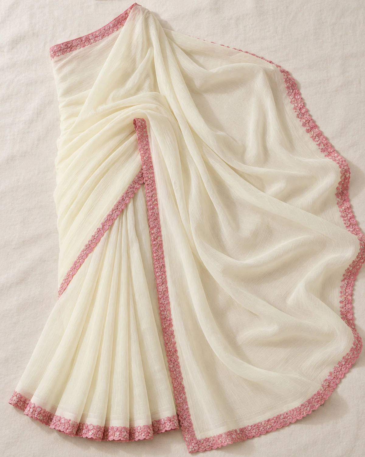 The ivory georgette saree laid flat on a cream cloth, showing its scalloped pink border