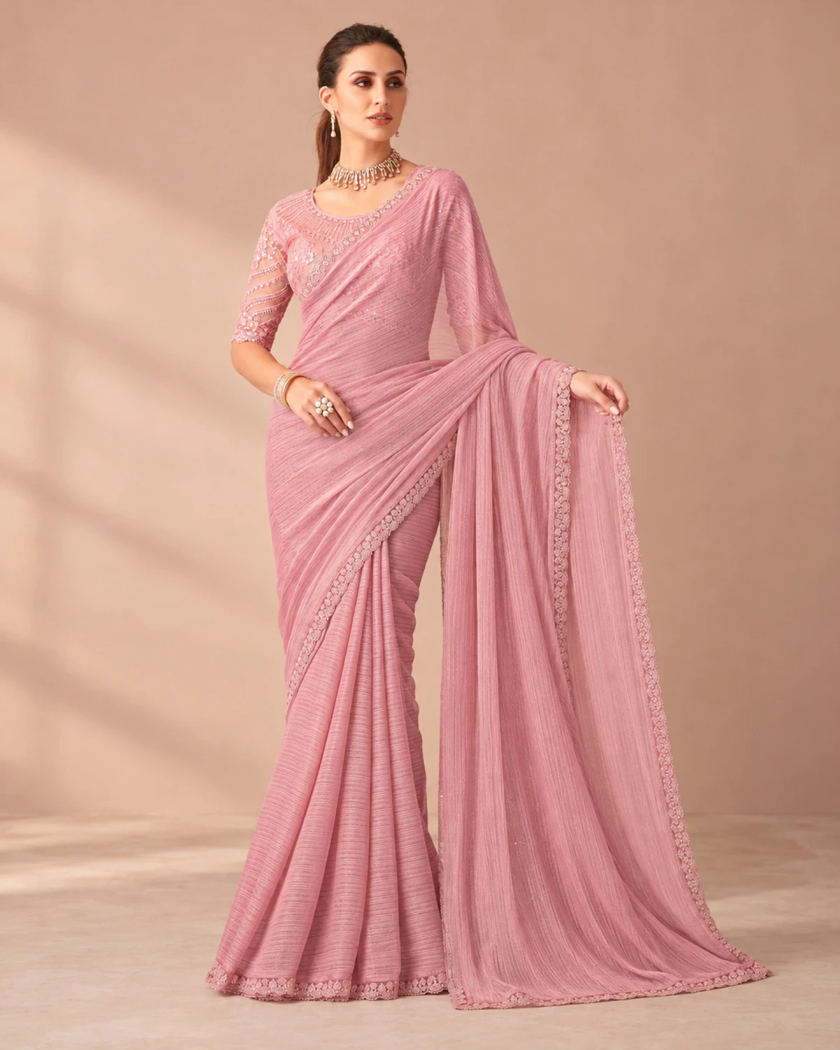 Woman holding out the pallu of the blush pink georgette saree in a softly lit room