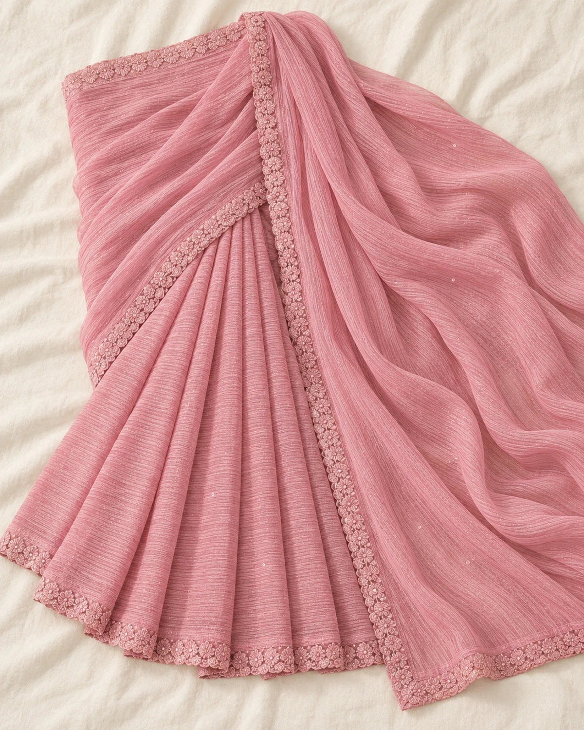 The blush pink georgette saree laid flat on a cream cloth, showing its scalloped border
