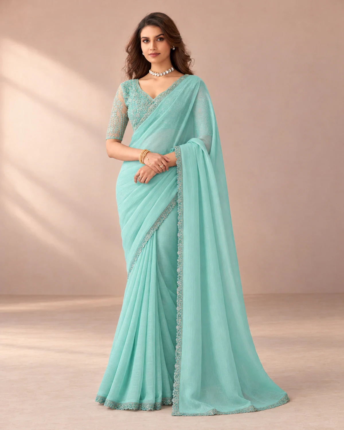 Woman wearing an aqua blue textured georgette saree with a scalloped matching border, standing in a softly lit peach room