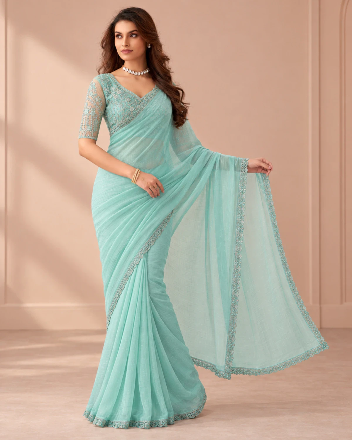 Woman holding out the pallu of the aqua blue georgette saree in a softly lit room