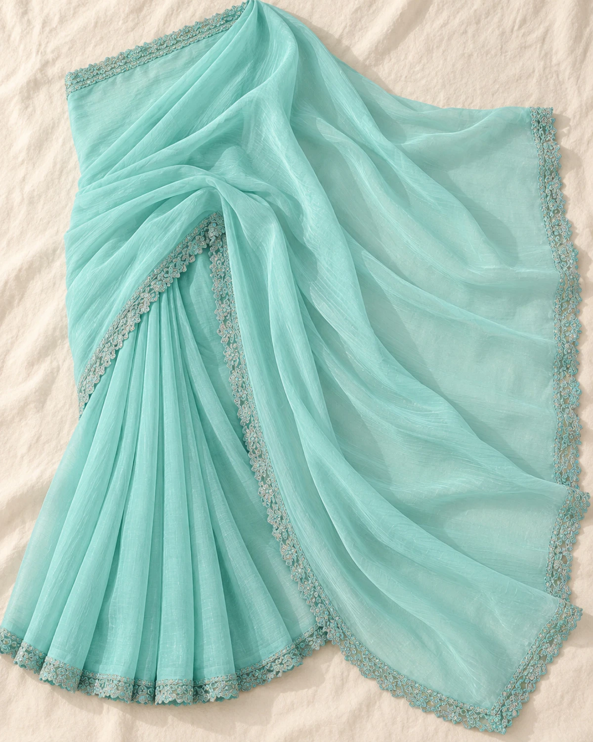 The aqua blue georgette saree laid flat on a cream cloth, showing its scalloped border