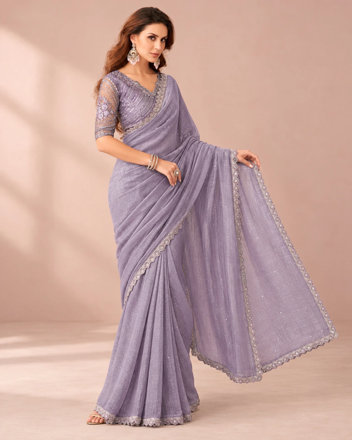Woman holding out the pallu of the lavender georgette saree in a softly lit room
