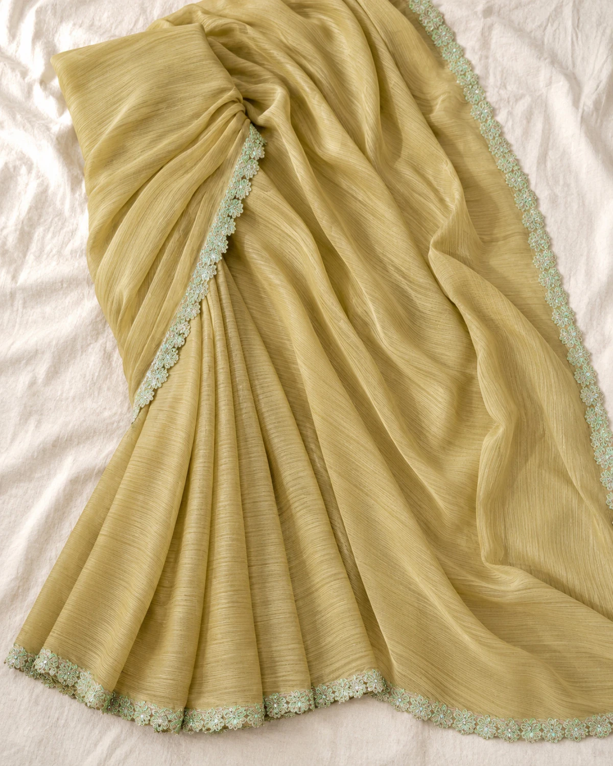 The olive beige georgette saree laid flat on a cream cloth, showing its scalloped mint green border