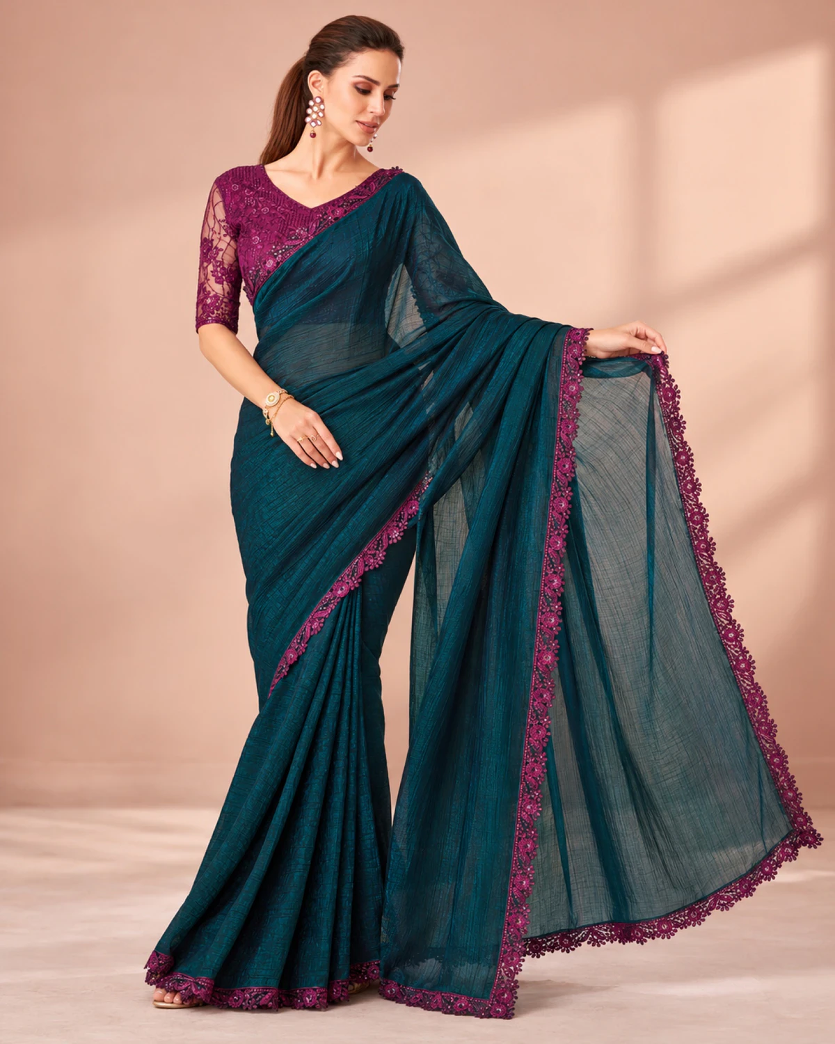 Woman holding out the pallu of the deep teal peacock rainbow saree in a softly lit room
