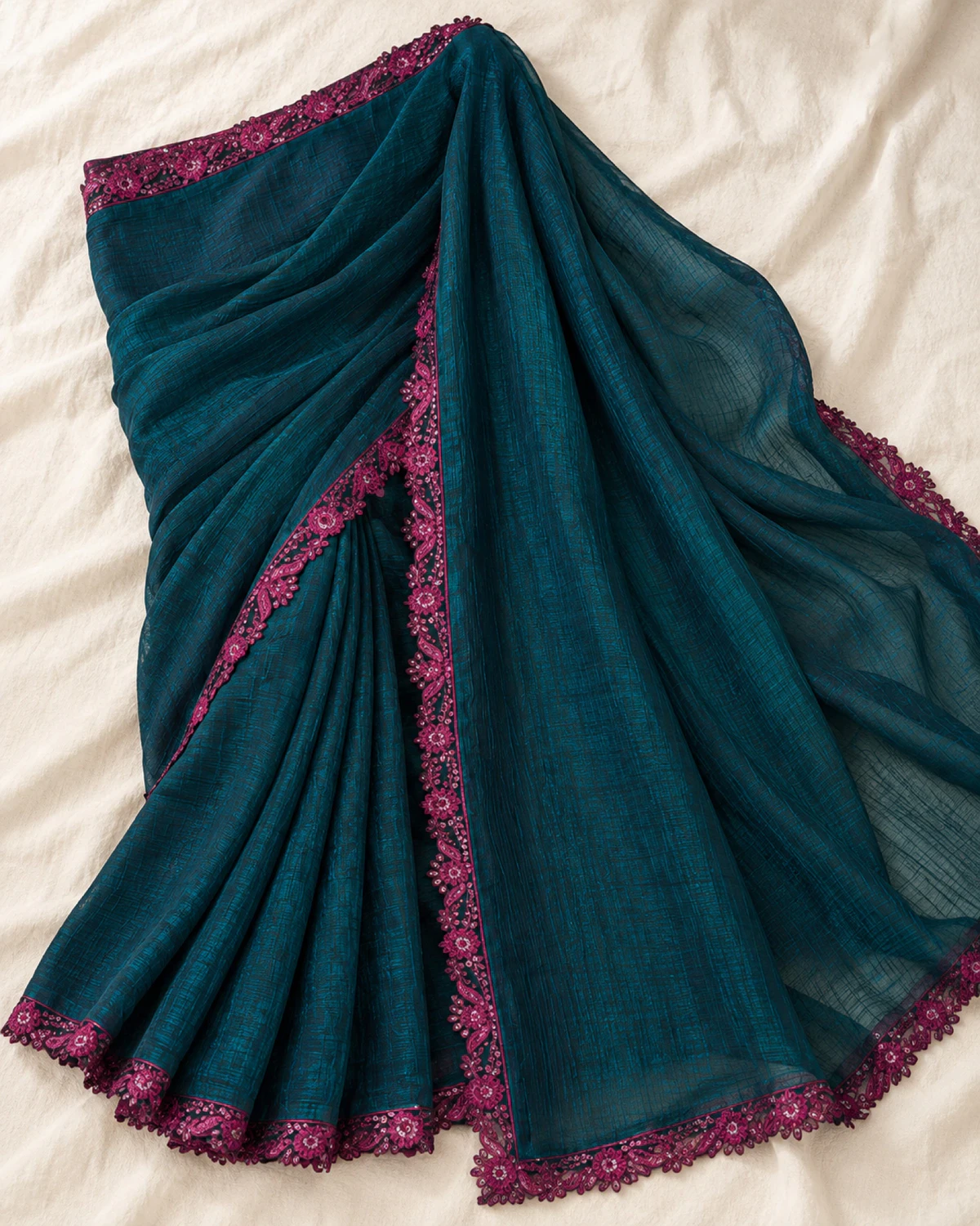 The deep teal peacock rainbow saree laid flat on a cream cloth, showing its scalloped magenta border