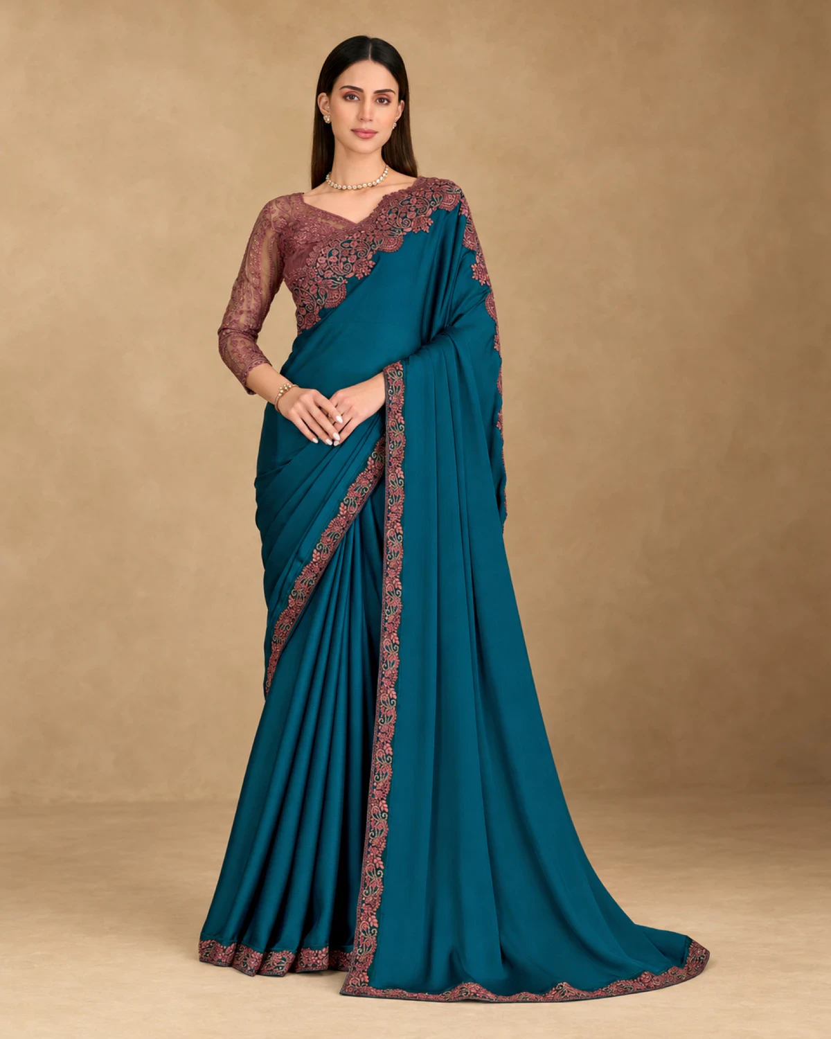 Woman wearing a teal satin chiffon saree with a wine embroidered border, standing against a warm beige backdrop
