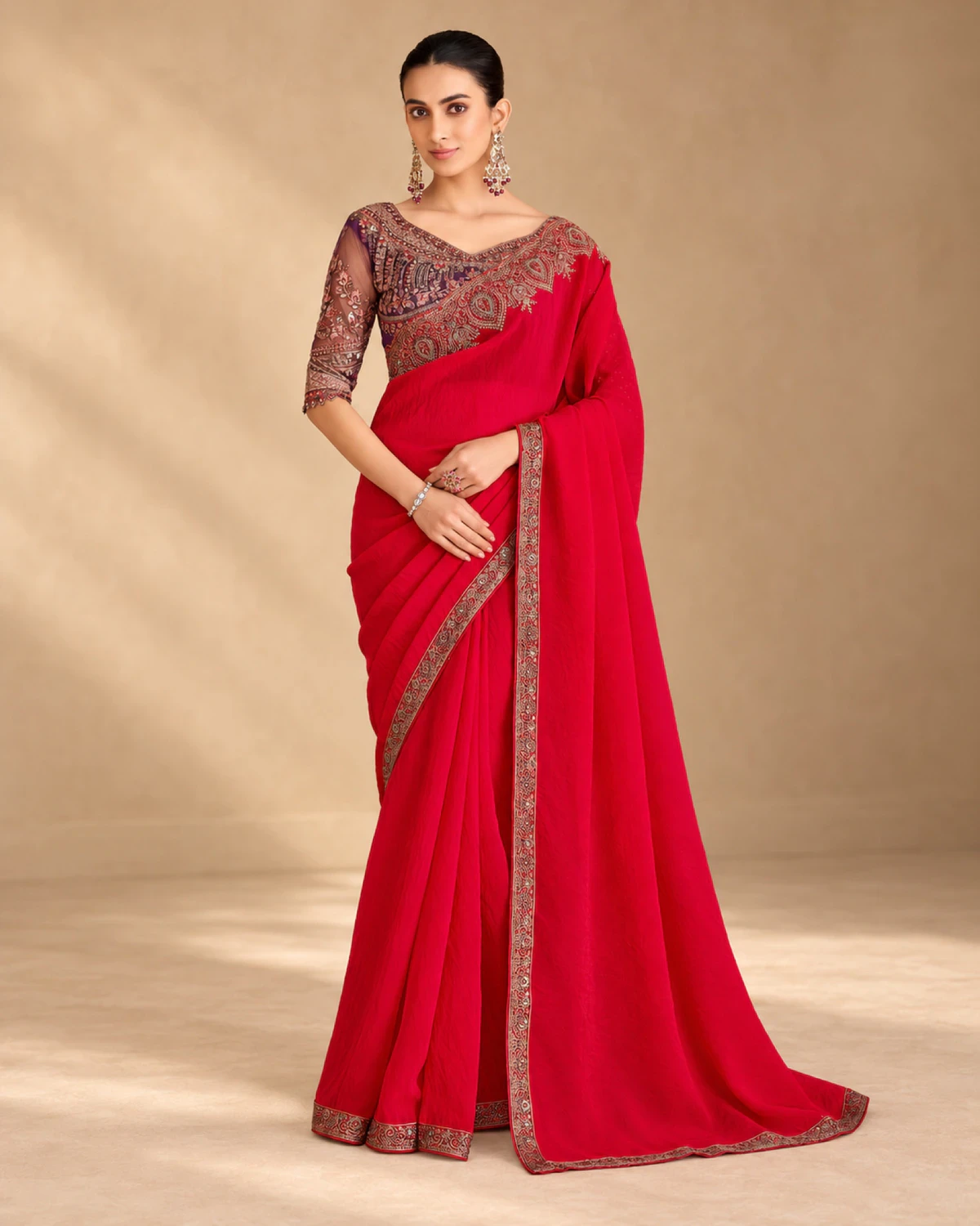 Woman wearing a red satin georgette saree with a gold embroidered border, standing against a warm beige backdrop