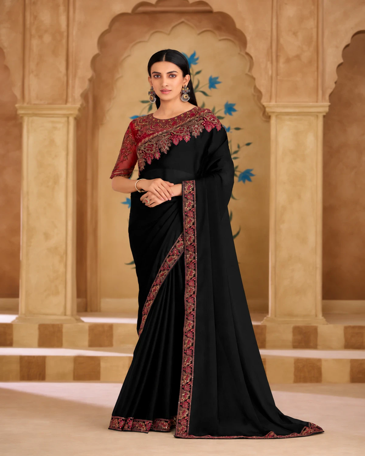 Woman wearing a black georgette silk saree with a red embroidered border, standing under carved arches