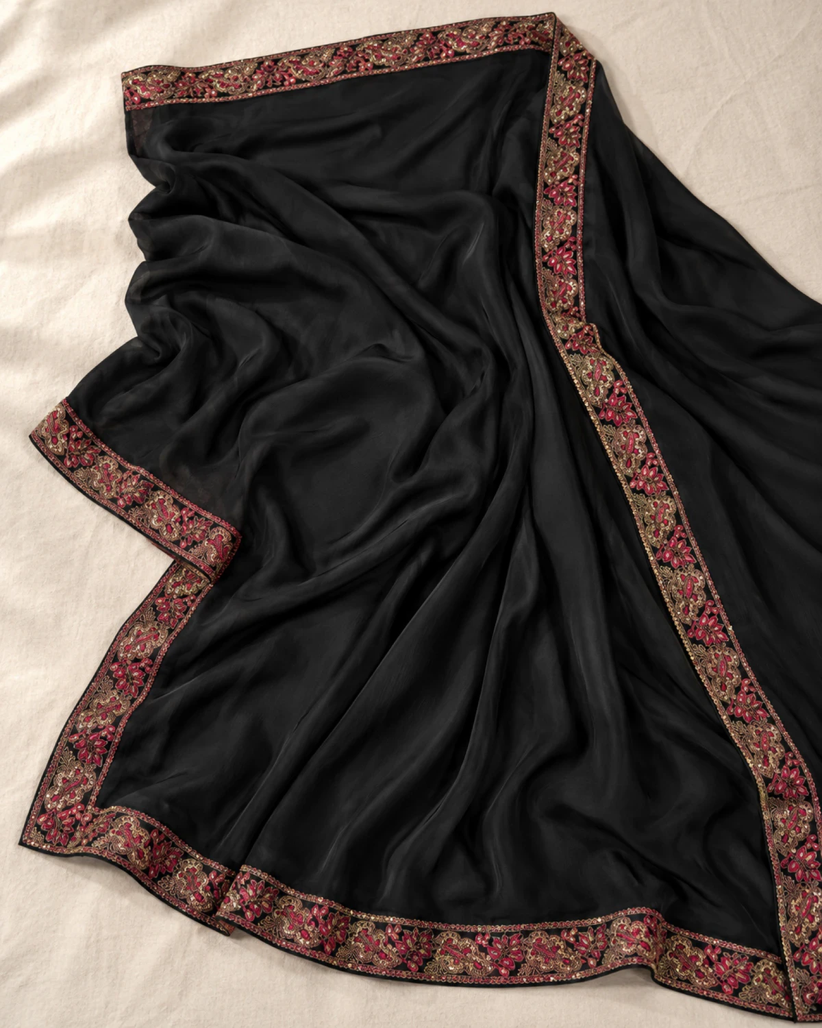 The black georgette silk saree laid flat on a cream cloth, showing its red embroidered border