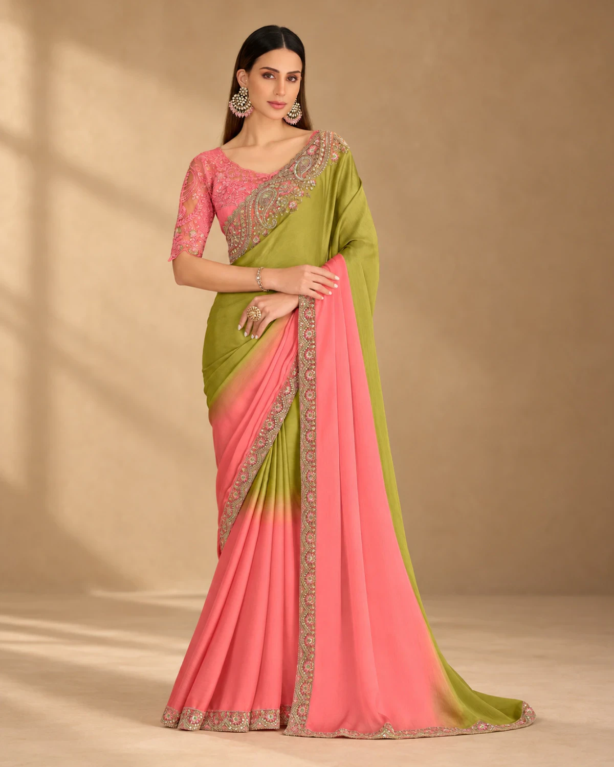 Woman wearing an olive and pink shaded crush georgette saree with an embroidered border, standing against a warm beige backdrop