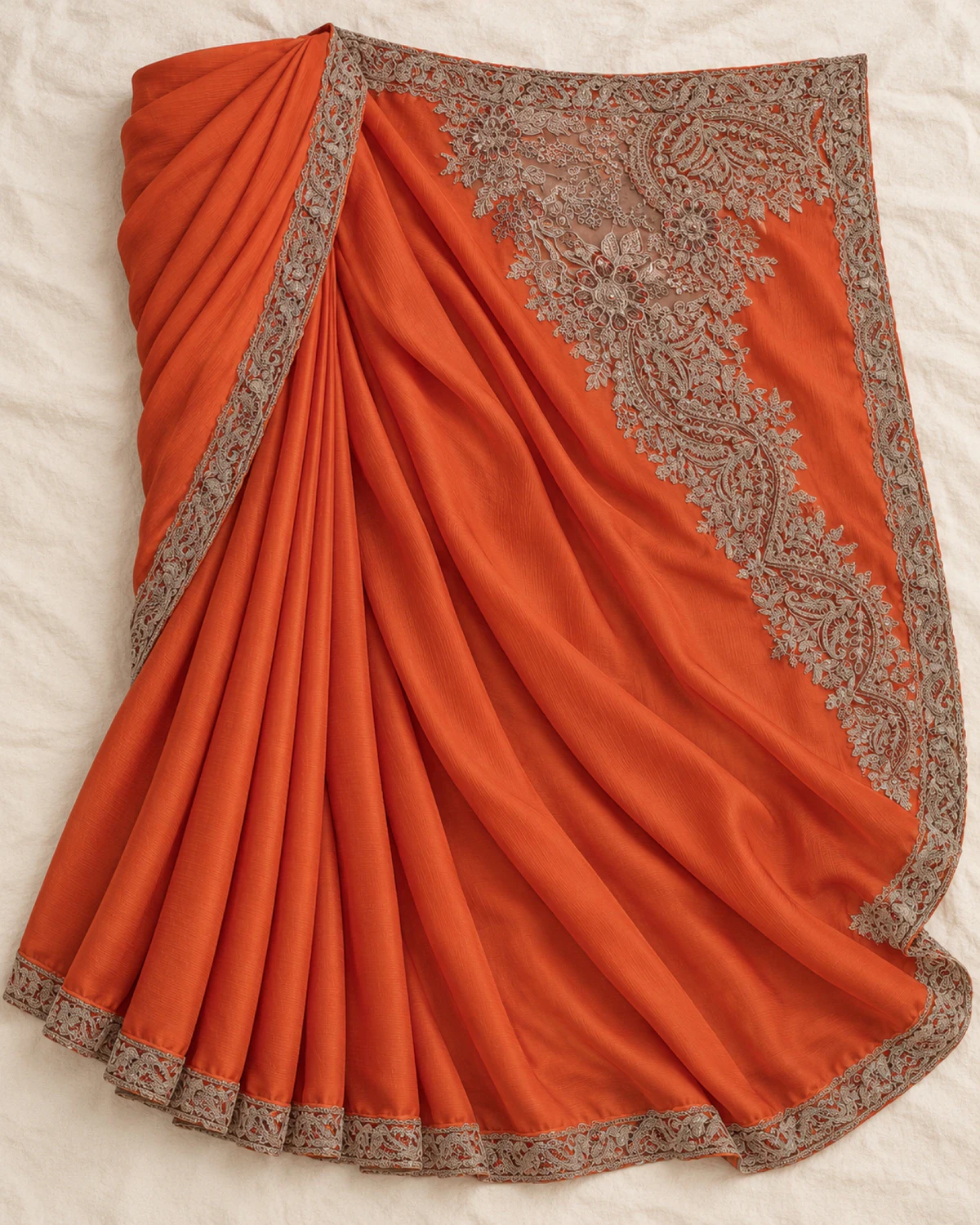 The rust satin chiffon saree laid flat on a cream cloth, showing its embroidered border and pallu