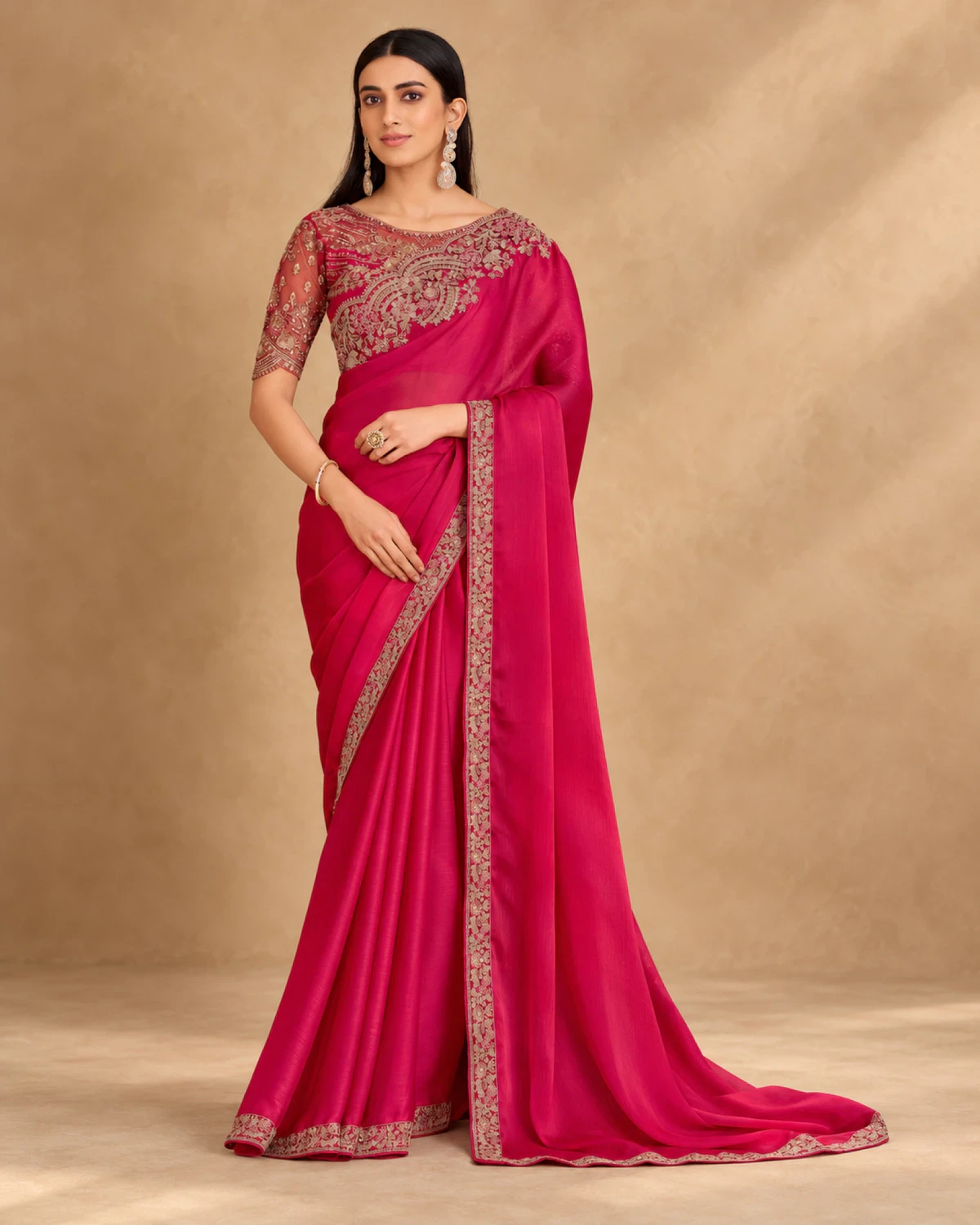 Woman wearing a rani pink satin chiffon saree with a gold embroidered border, standing against a warm beige backdrop