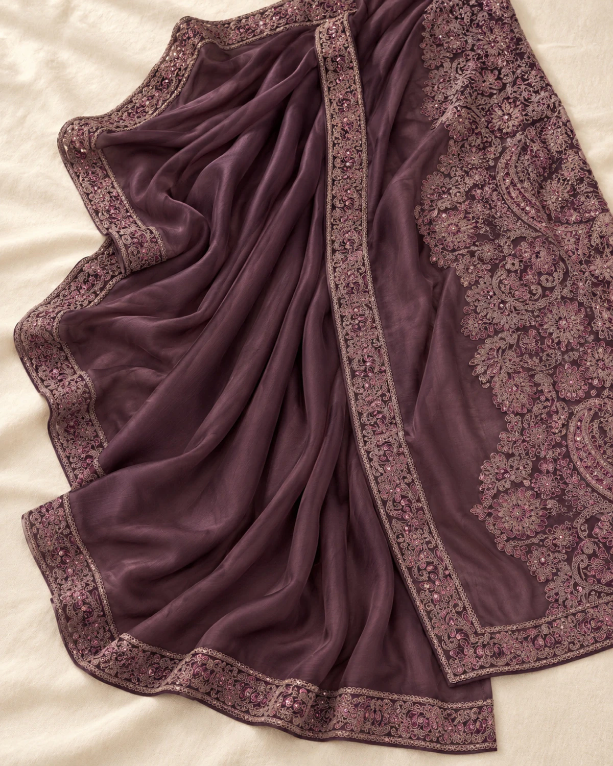 The plum satin chiffon saree laid flat on a cream cloth, showing its embroidered border and pallu