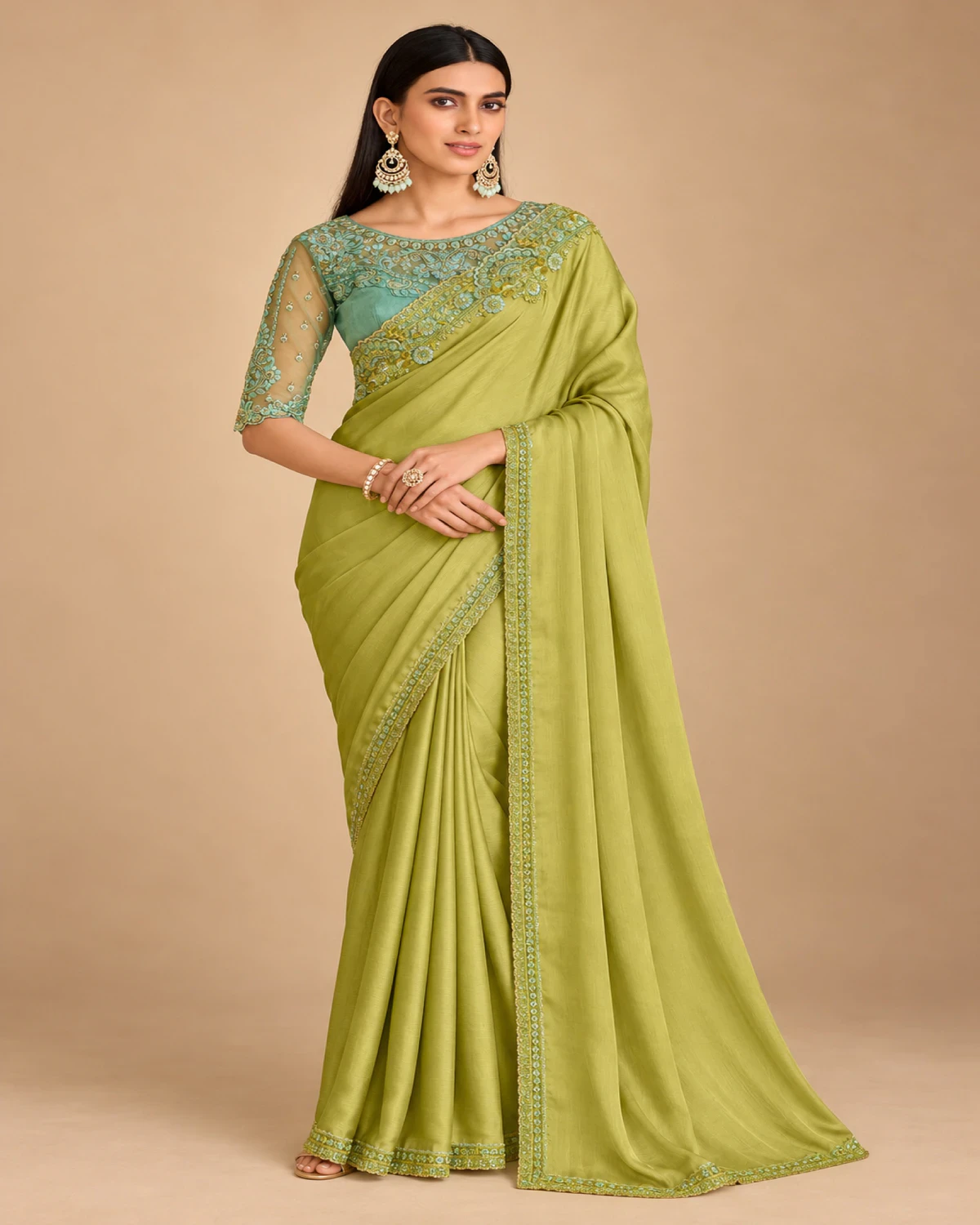 Woman wearing a lime green satin chiffon saree with a sea green embroidered border, standing against a warm beige backdrop