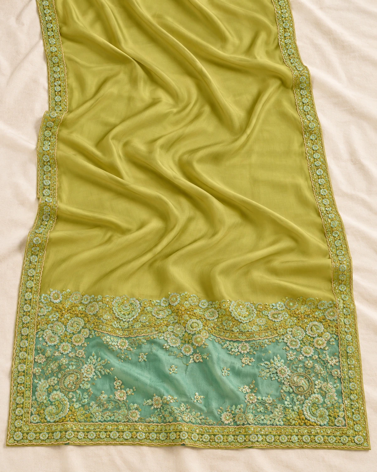 The lime green satin chiffon saree laid flat on a cream cloth, showing its embroidered border