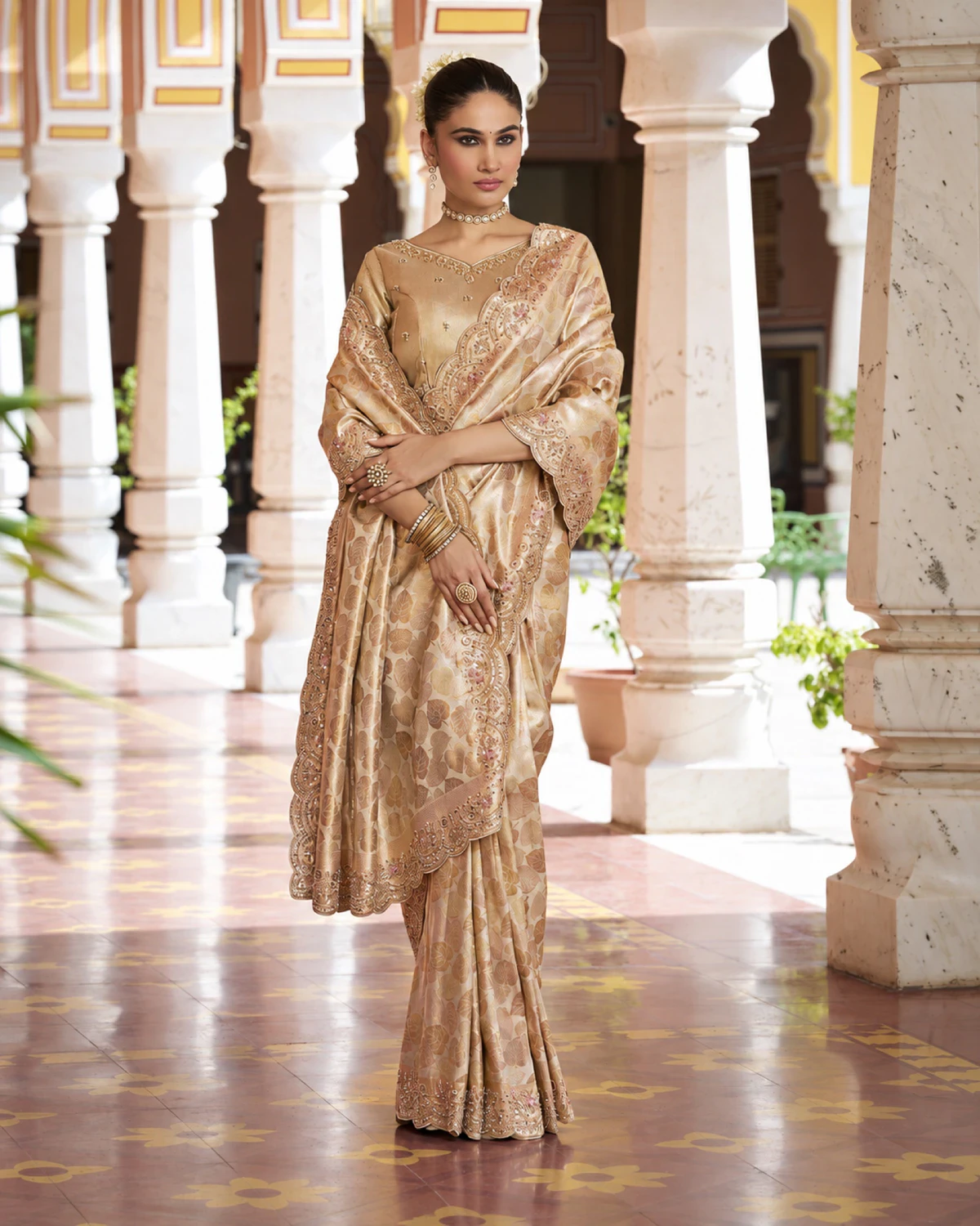 Woman in the champagne gold soft silk saree with its pallu wrapped across the front, in a pillared courtyard