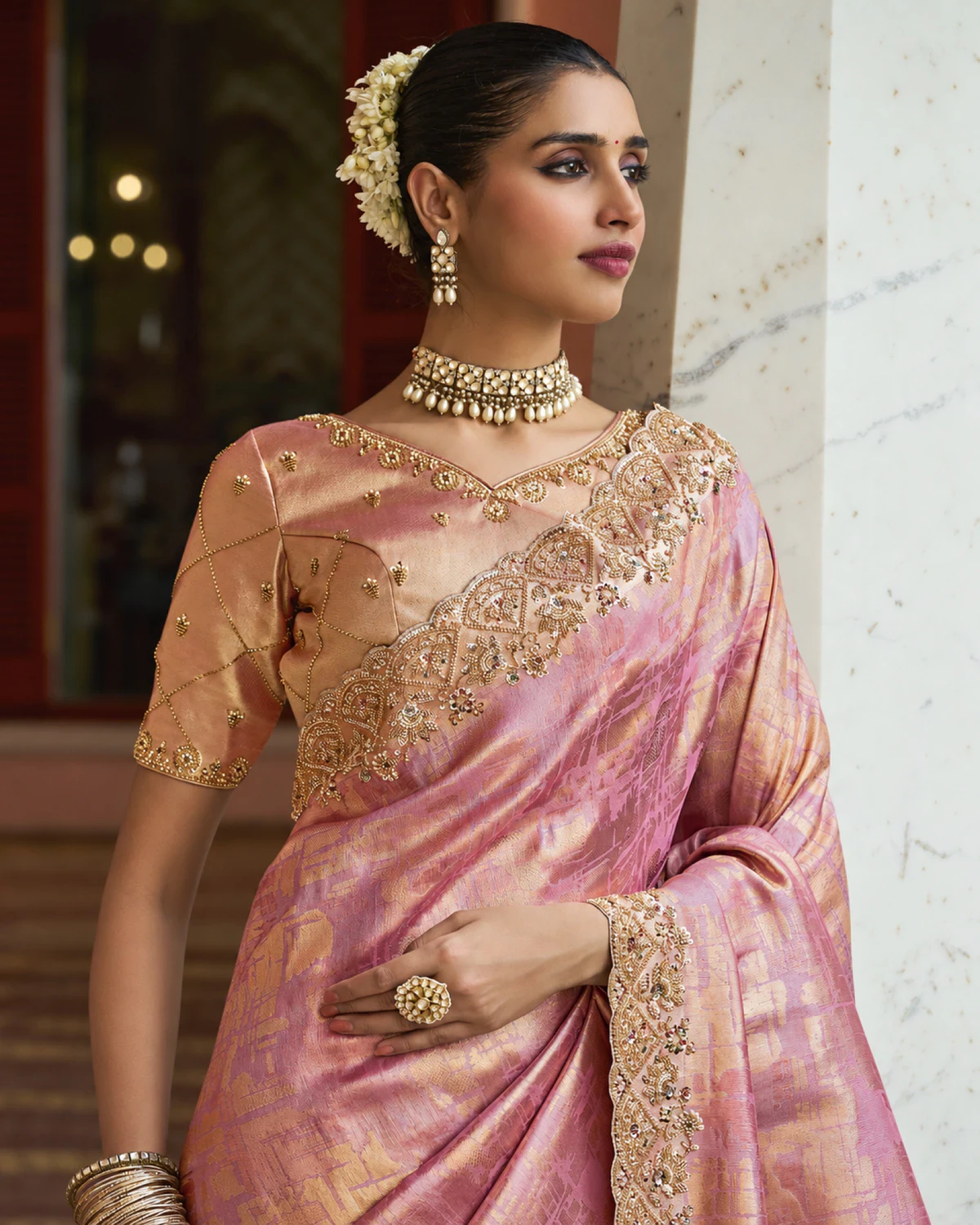 Close-up of a woman in the rose pink soft silk saree, showing its beaded border and peach-gold blouse