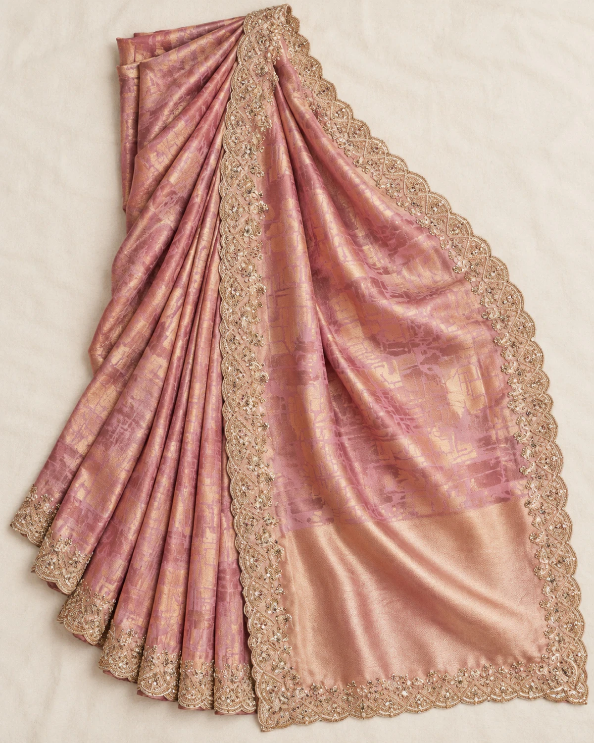 The rose pink soft silk saree laid flat on a cream cloth, showing its gold woven pattern, beaded border and gold pallu end