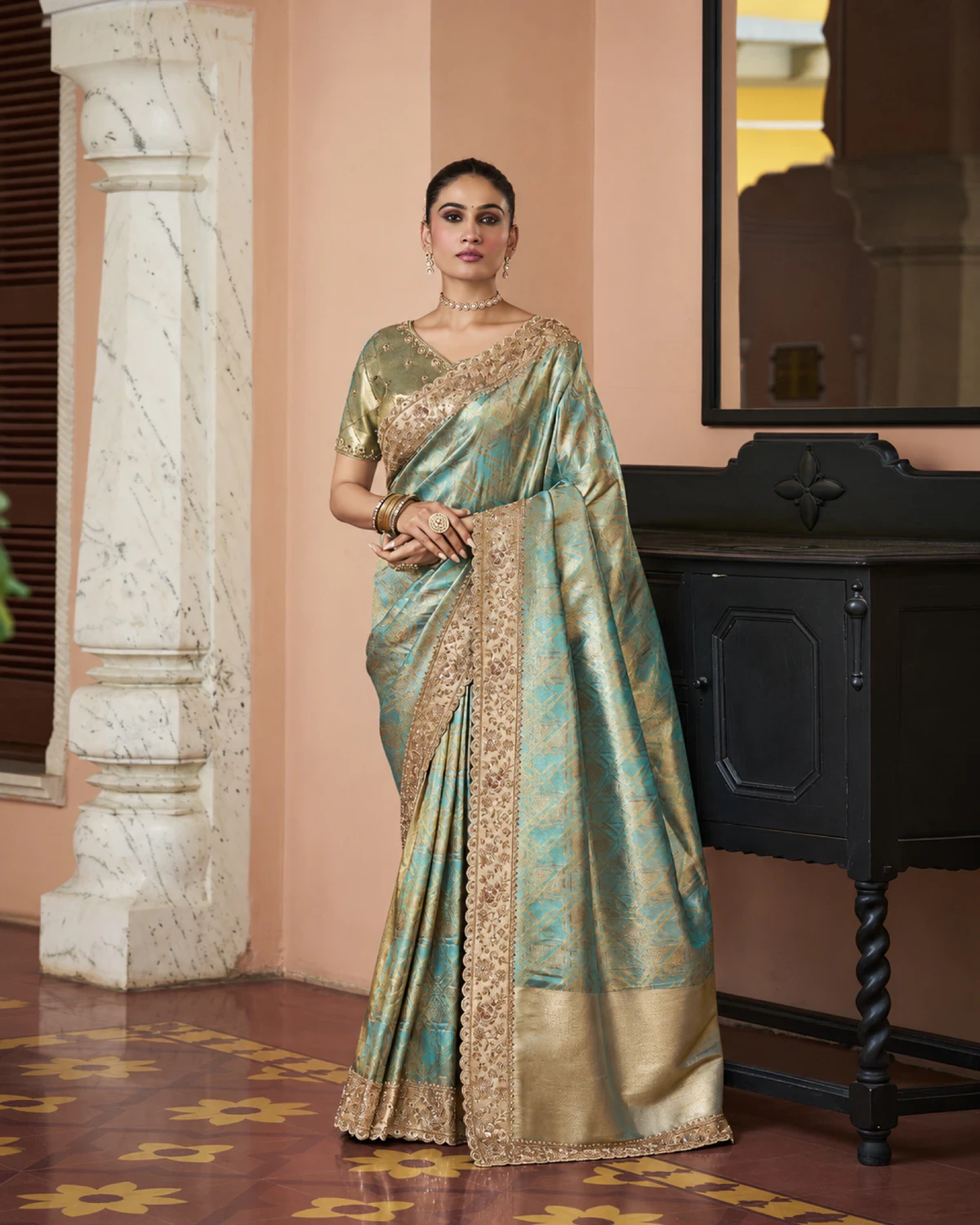 Woman in the aqua soft silk saree beside a black cabinet, its plain gold pallu end showing