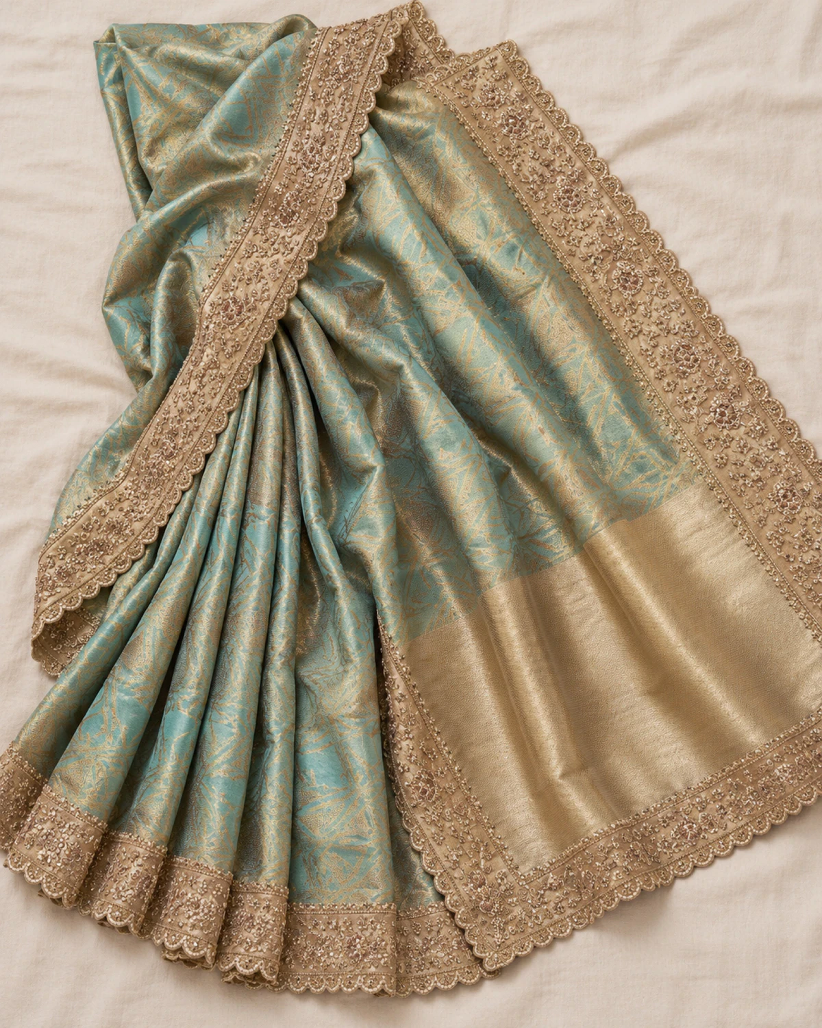 The aqua soft silk saree laid flat on a cream cloth, showing its gold vines, scalloped border and gold pallu